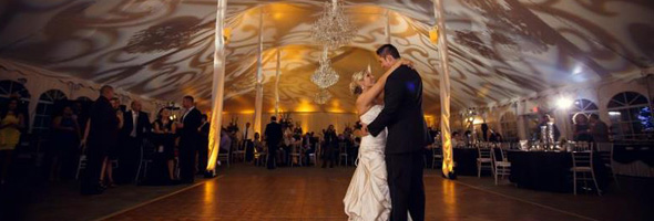 wedding couple dancing with event lighting gobos and amber uplighting in the background tent